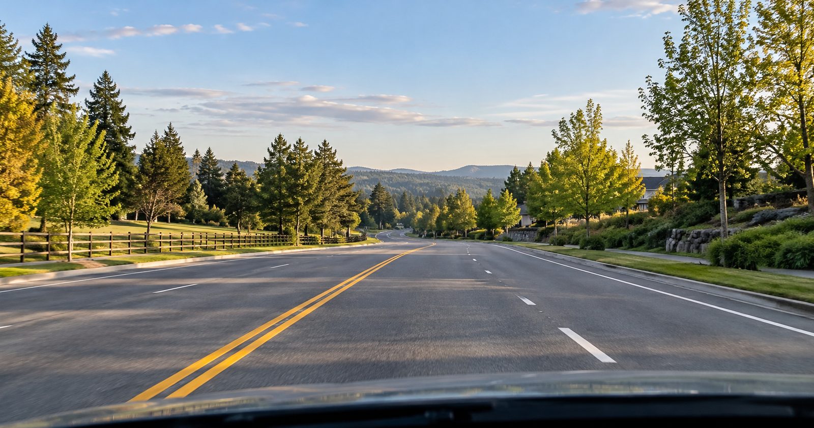 A wide, tree-lined road at golden hour, seen from the driver's seat.